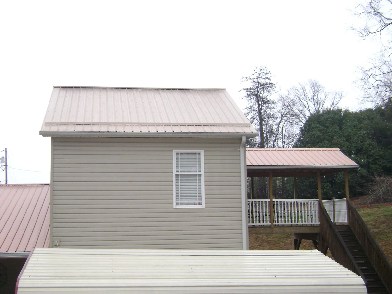 Tan metal roofs on a two story addition and attached porch, from a Roof Replacement job in Spring Hill